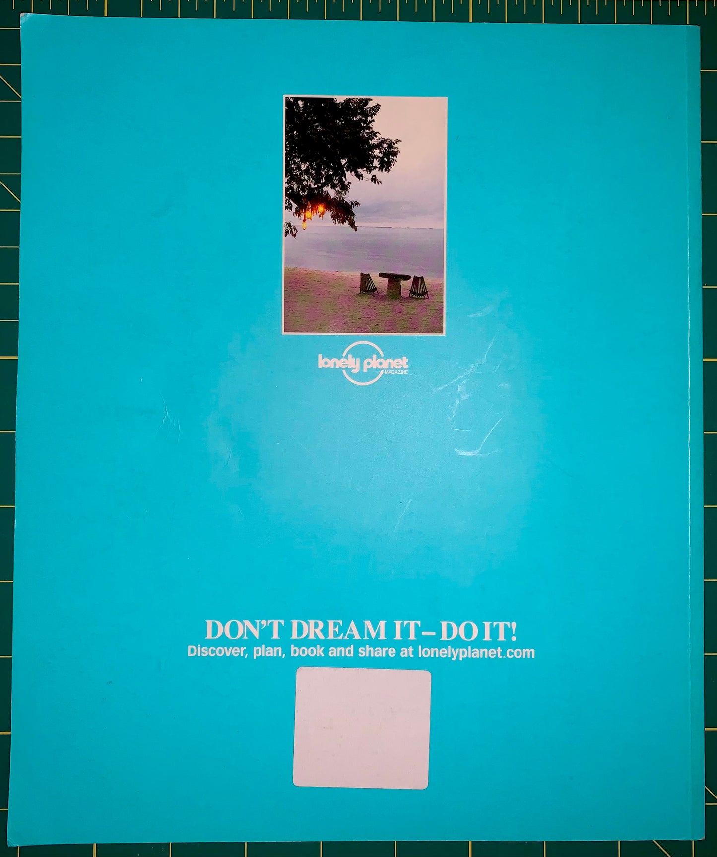 A vintage Lonely Planet travel guide cover in bright turquoise blue, featuring the iconic 'DON'T DREAM IT - DO IT!' slogan and a small central photograph of a lakeside bench. The cover is laid flat on a green cutting mat.
[additional_image_link]