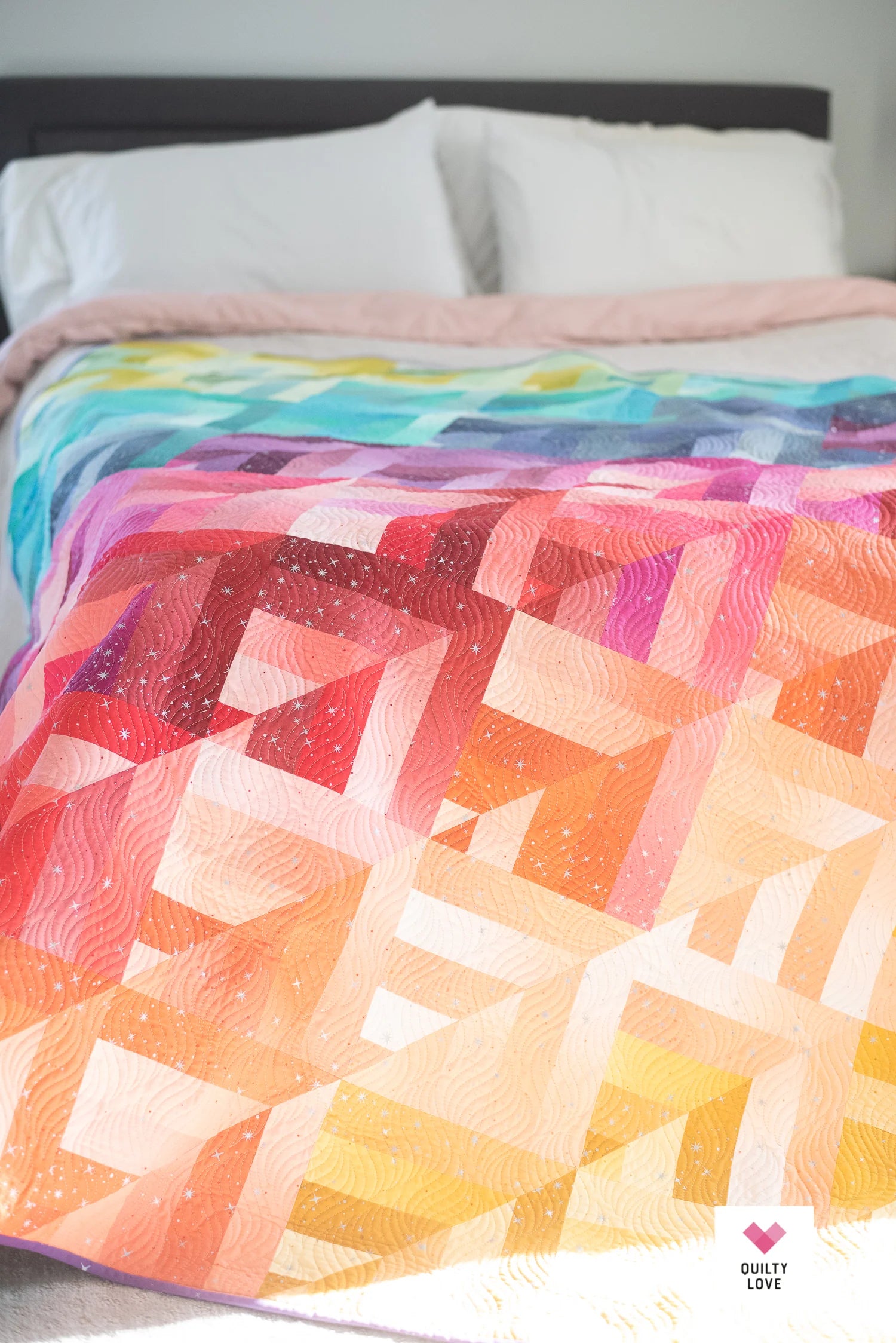 Colorful quilt with geometric pattern on a bed.
Photo by Quilty Love [additional_image_link]