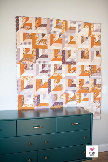 Quilt with geometric pattern hanging above a teal dresser.
Photo by Quilty Love [additional_image_link]