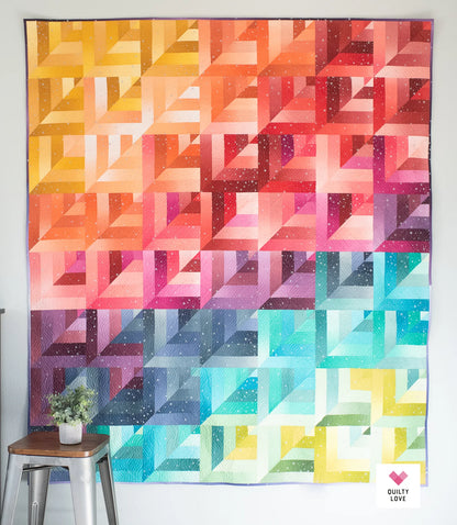 Colorful geometric quilt hanging on a wall with a plant and stool in the foreground.
Photo by Quilty Love [additional_image_link]