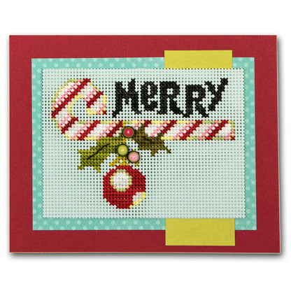 A square handmade cross-stitch card featuring a festive holiday design with the word 'MERRY' in black, a candy cane, holly leaves, and a red ornament on white stitched fabric, bordered by light blue and yellow strips and a red outer border.
Photo by JustAnotherButtonCompany.com [additional_image_link]