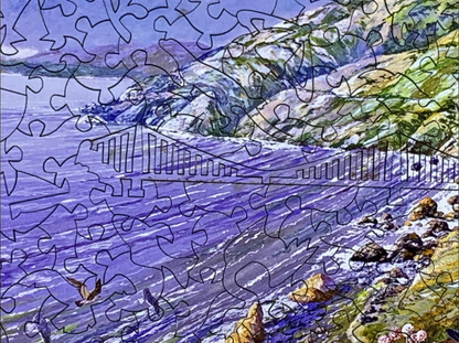 A completed jigsaw puzzle depicting a colorful coastal landscape with purple water, green hills, flying birds, and wildflowers in the foreground.
Photo by Nautilus Puzzles [additional_image_link]
