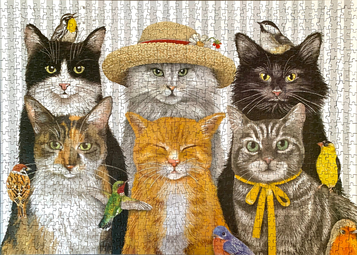 A completed jigsaw puzzle featuring a group portrait of six cats with small birds perched on them, set against a light patterned background.
Photo by Karen King [additional_image_link]