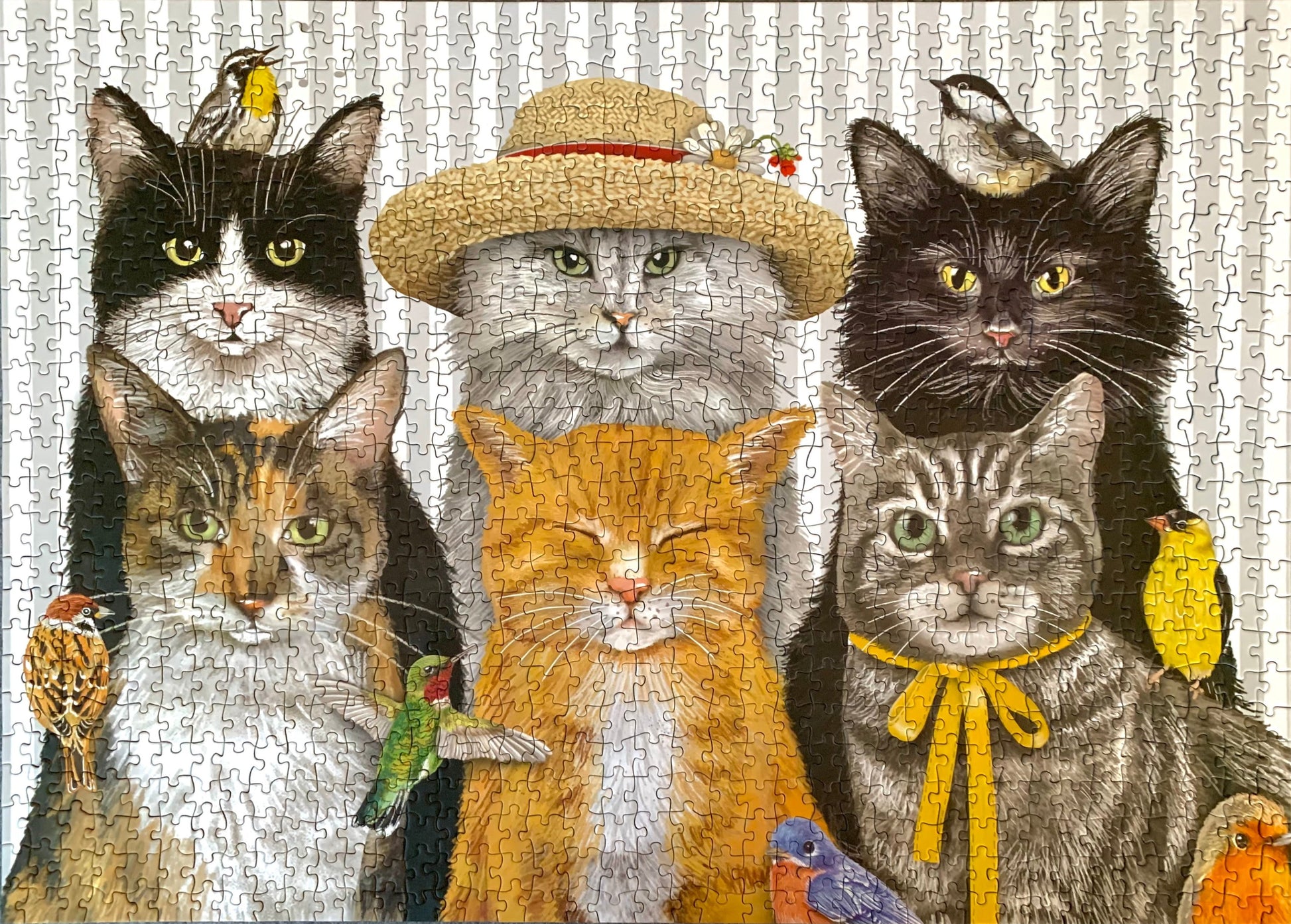 A completed jigsaw puzzle featuring a group portrait of six cats with small birds perched on them, set against a light patterned background.
Photo by Karen King [additional_image_link]