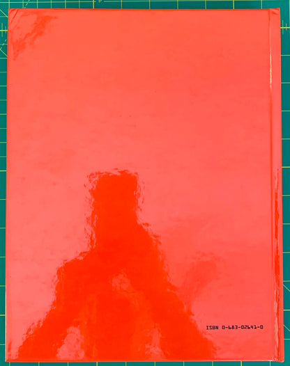 A glossy, bright orange-red book cover with a visible spine on the right, photographed flat against a green cutting mat with grid lines. Small black text in the bottom right corner reads 'ISBN 0-483-02641-0'.
[additional_image_link]