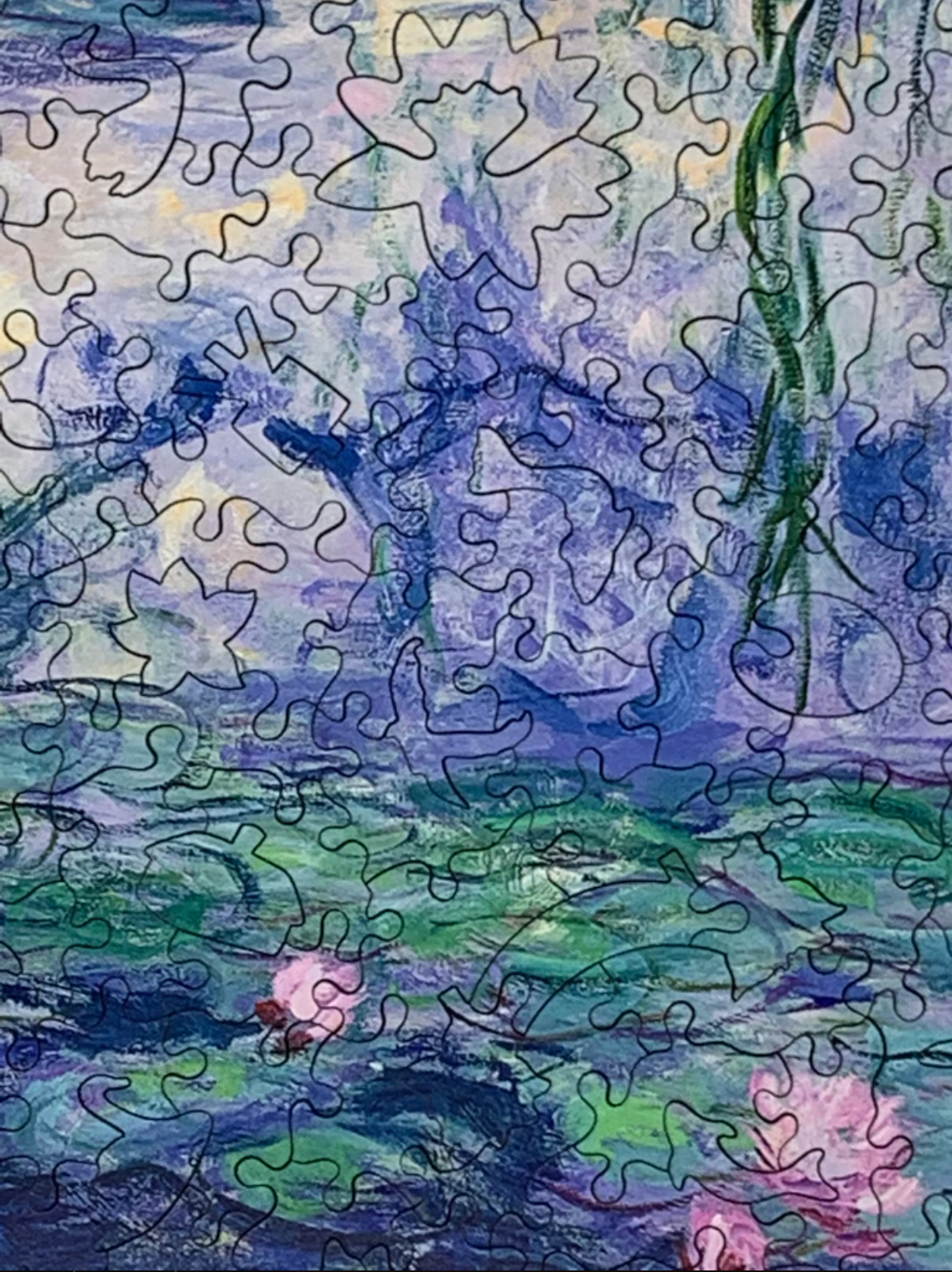 A jigsaw puzzle depicting a section of Claude Monet's famous waterlily paintings, featuring green lily pads and pink flowers in a blue pond.
Photo by Nautilus Puzzles [additional_image_link]