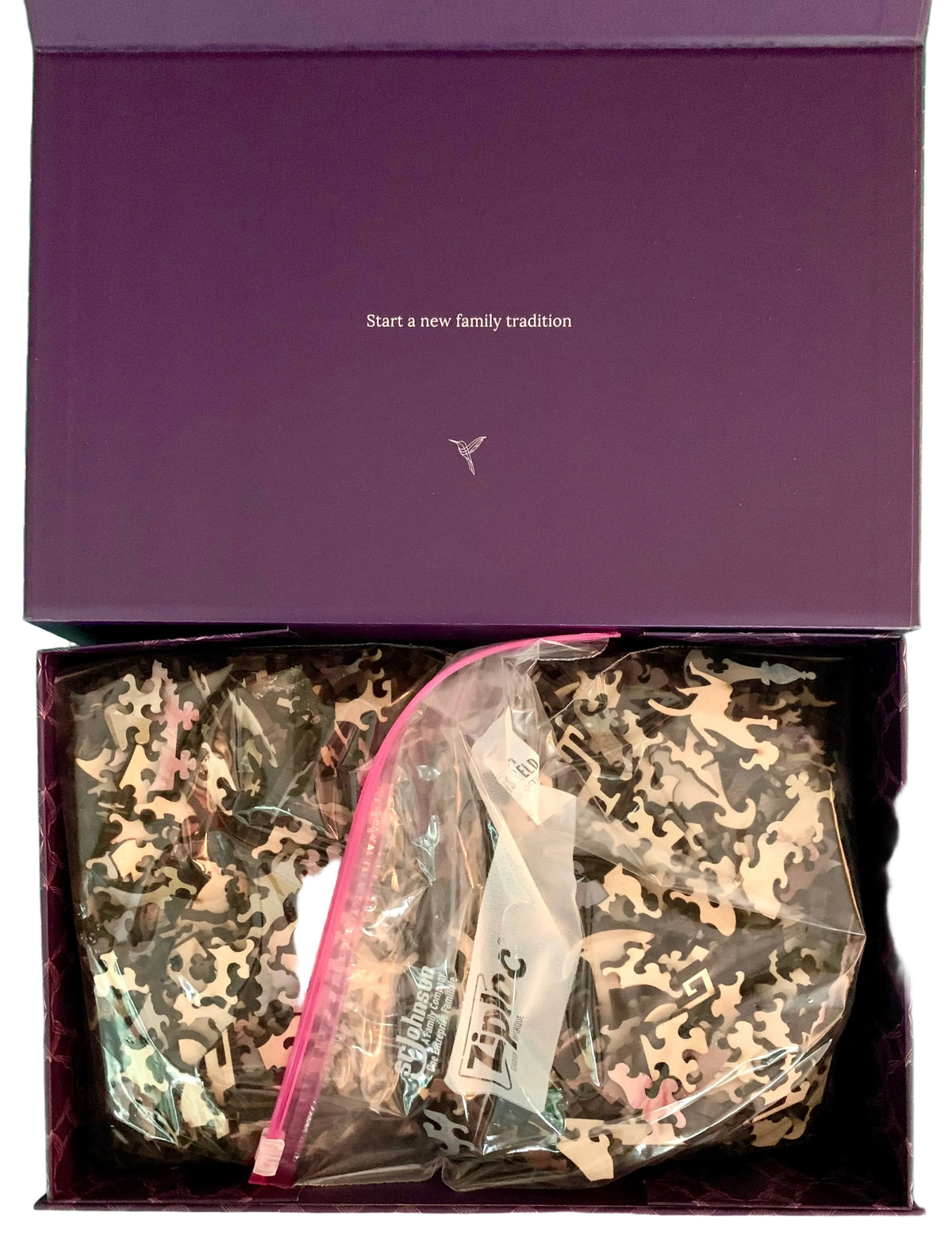 An open purple box containing two clear plastic bags filled with camouflage-patterned fabric pieces. The inside lid has small white text and a small logo.
Photo by Karen King [additional_image_link]