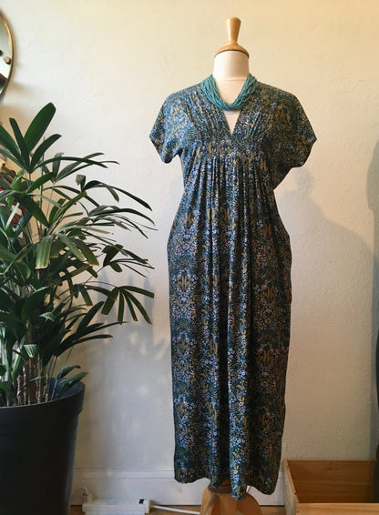 Long patterned dress on a mannequin against a white wall with a plant to the left.
[additional_image_link]