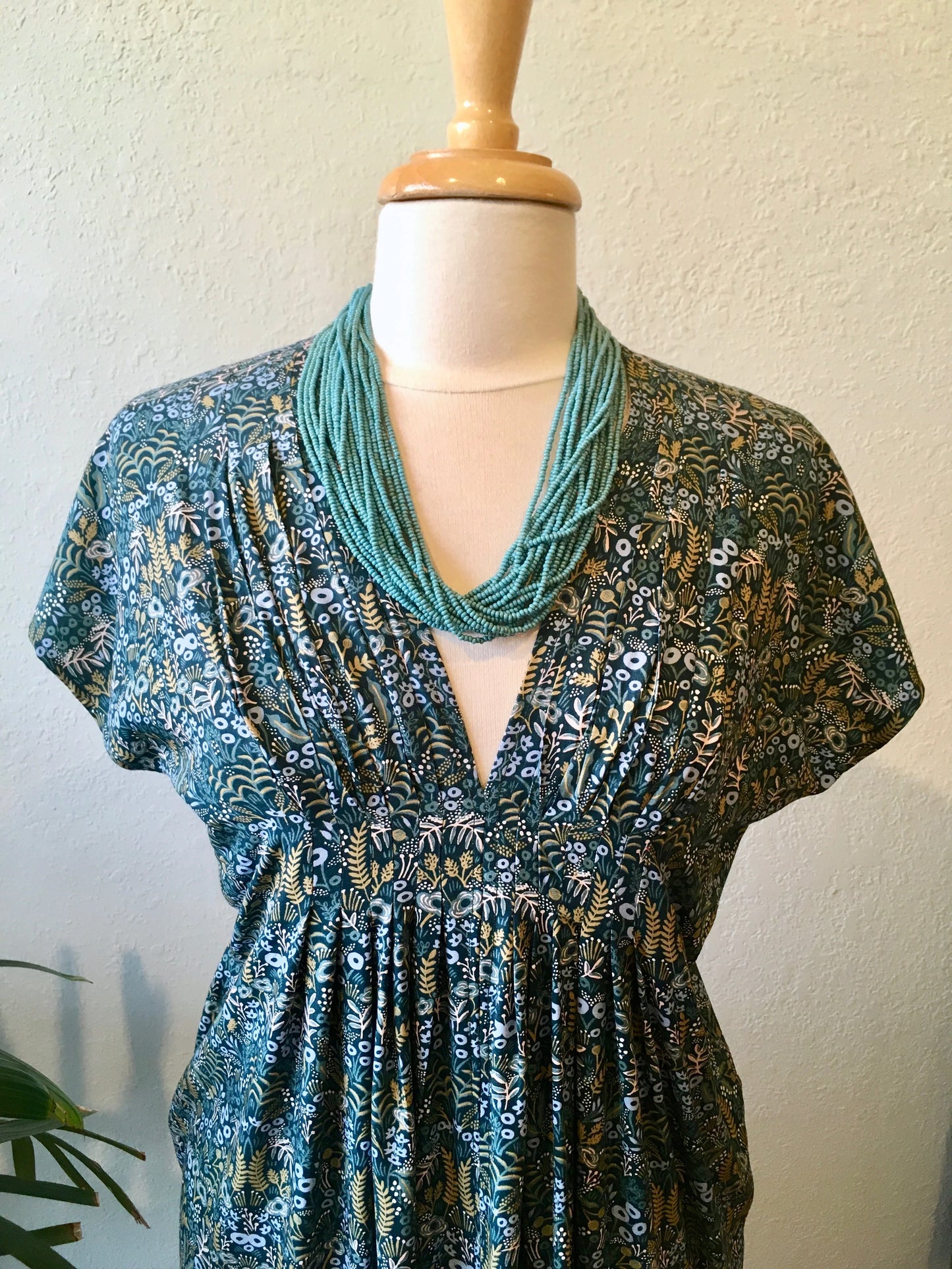 Mannequin wearing a blue floral dress with a green scarf on a plain background.
[additional_image_link]