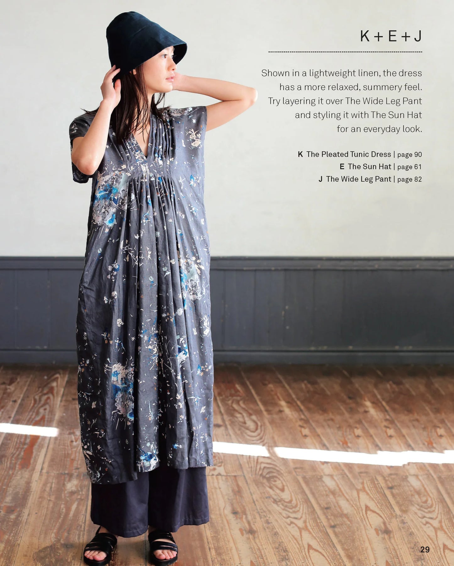 Woman wearing a pleated tunic dress with text on a gray wall background.
[additional_image_link]