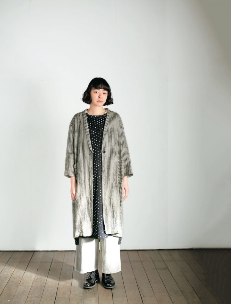 Person wearing a long, patterned coat over a dress with a plain background.
[additional_image_link]