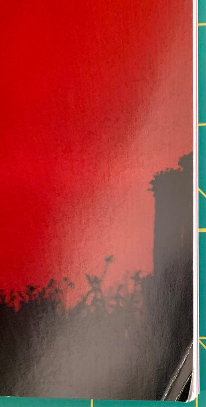 A close-up of a notebook or book cover featuring a textured red top half and a dark gray silhouette landscape on the bottom half, with a green cutting mat edge visible on the right side.
[additional_image_link]