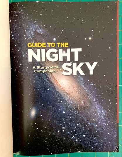 A book titled 'Guide to the Night Sky: A Stargazers Companion' lying on a green cutting mat. The cover features a starry night sky with a prominent spiral galaxy.
[additional_image_link]