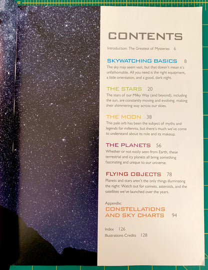 A printed contents page from a book or magazine, showing chapter titles and page numbers in blue and orange text on a cream page, placed on top of a dark blue starry sky photograph. The page is laid on a green grid cutting mat.
[additional_image_link]