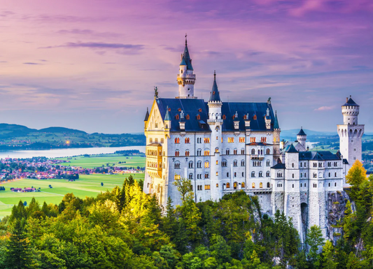 A completed jigsaw puzzle showing a scenic view of Neuschwanstein Castle in Germany, with a pink and purple sky, green trees, and the castle itself, photographed from above on a gray textured surface.
Photo by Nautilus Puzzles [image_link]