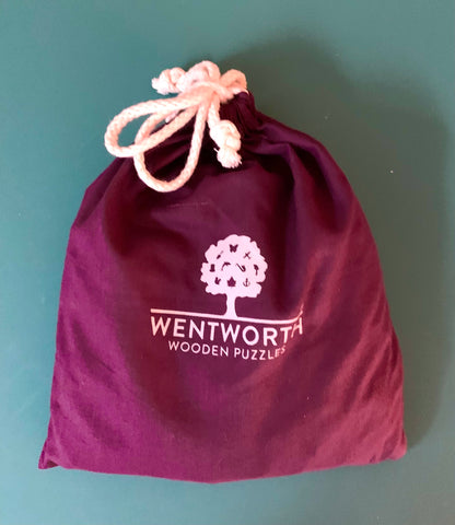 A deep purple drawstring pouch with a white printed Wentworth Wooden Puzzles logo, featuring a light pink drawstring, set against a solid teal background.
Photo by Karen King [additional_image_link]