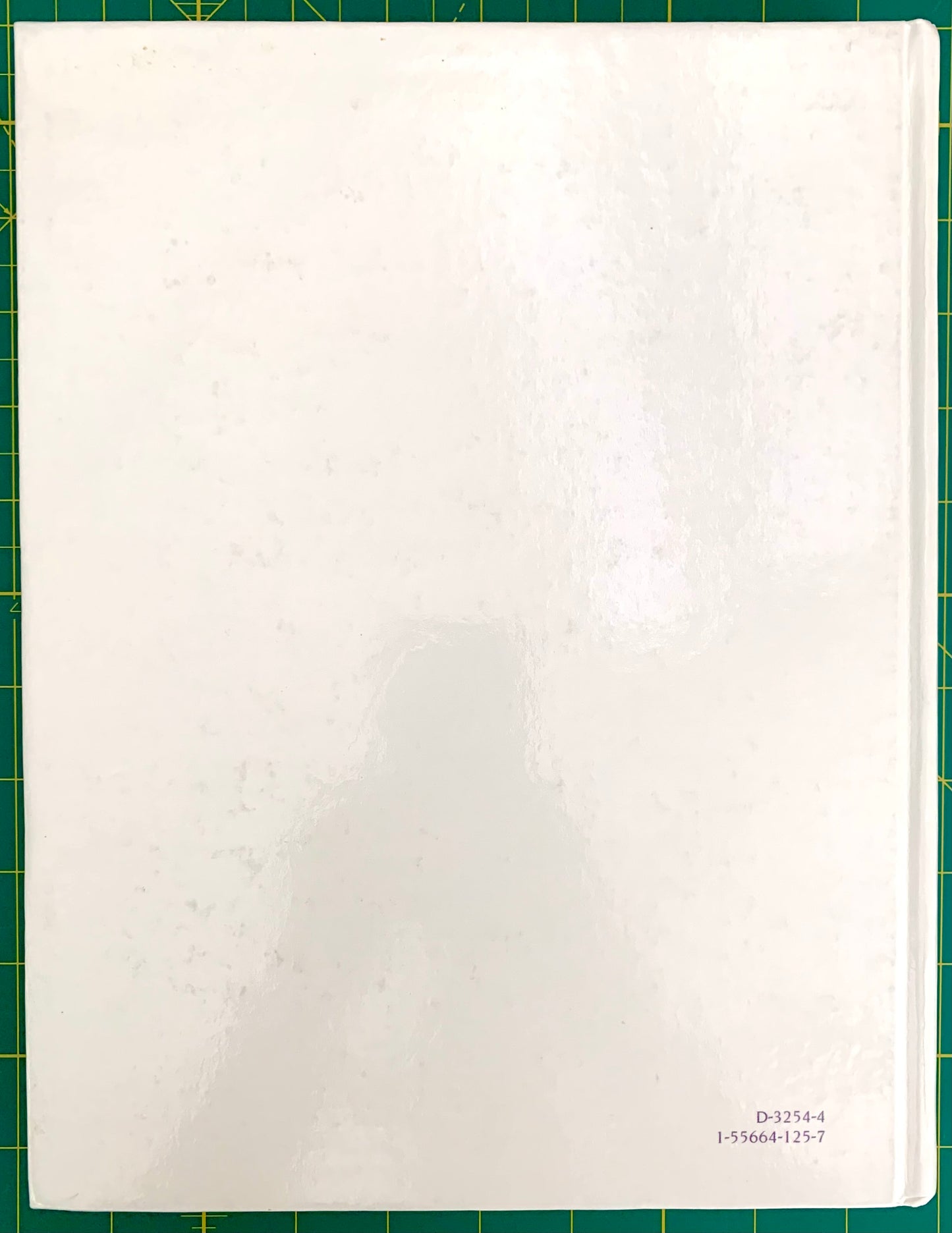A white rectangular back book cover with a glossy finish, photographed from above on a green cutting mat. Small printed alphanumeric text appears in the bottom-right corner of the sheet.
[additional_image_link]
