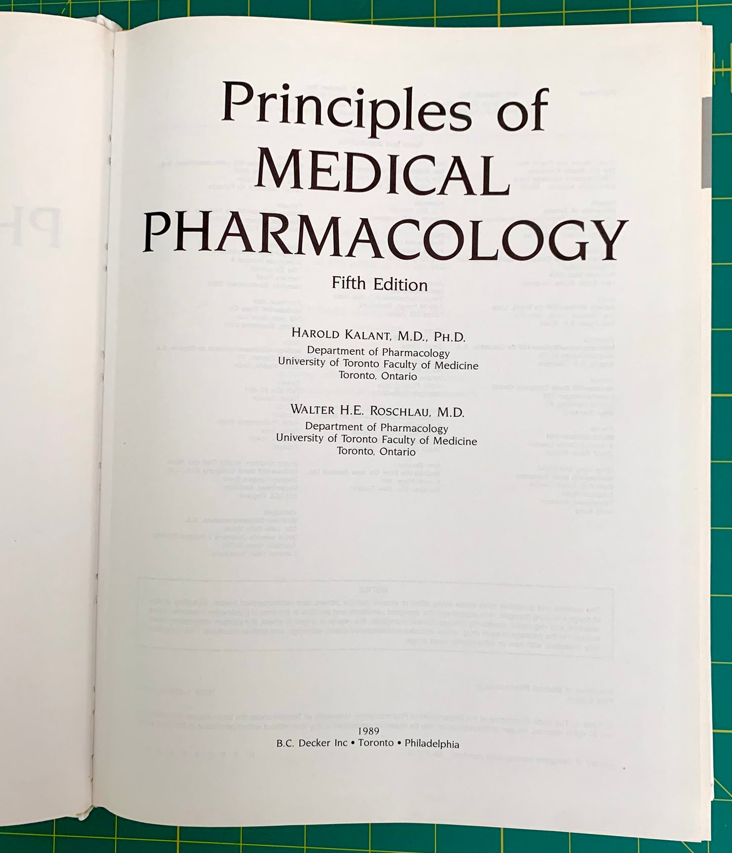 An open book showing the title page of 'Principles of Medical Pharmacology, Fifth Edition' on a green cutting mat background.
[additional_image_link]