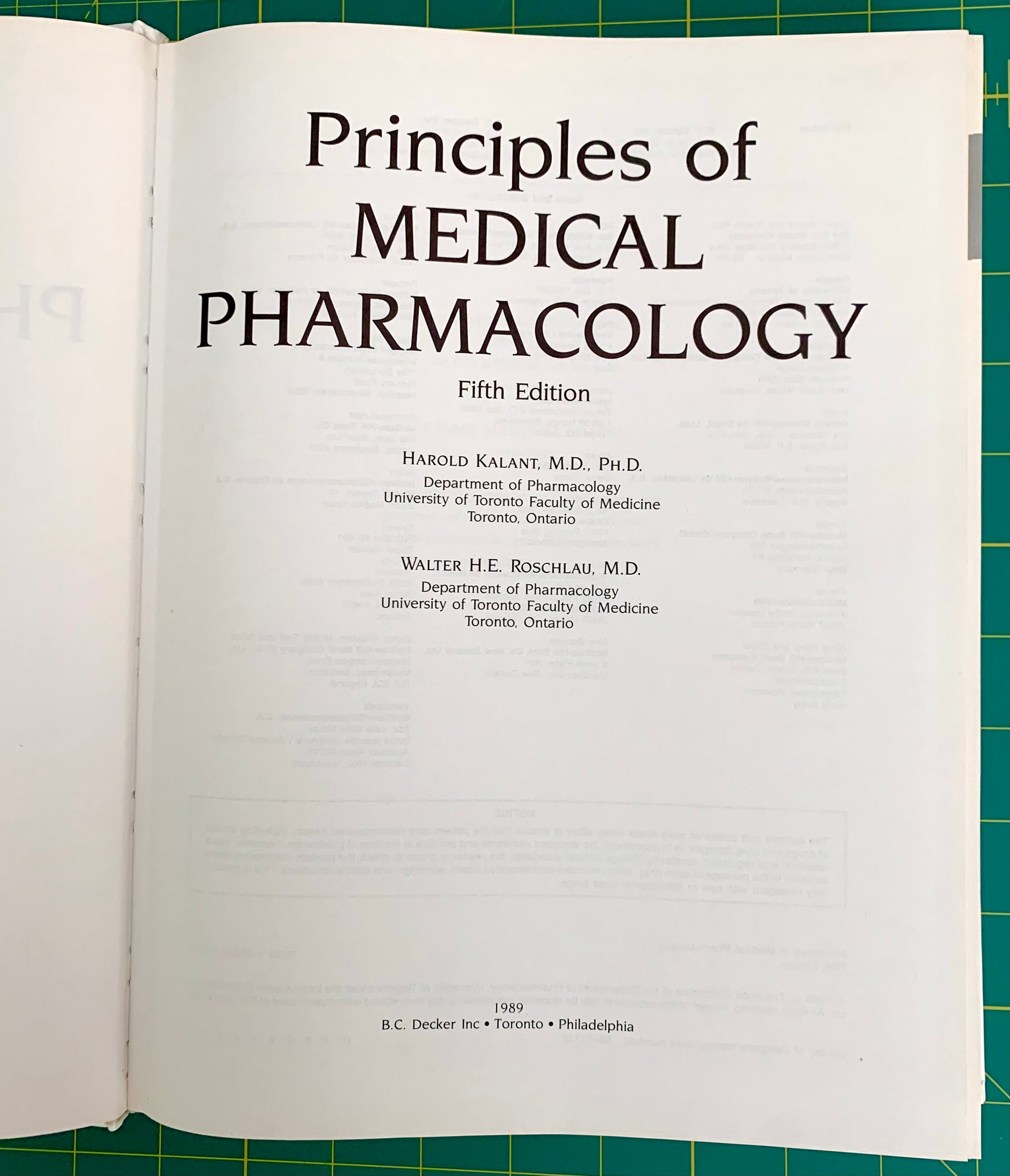 An open book showing the title page of 'Principles of Medical Pharmacology, Fifth Edition' on a green cutting mat background.
[additional_image_link]