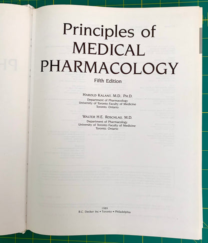An open book showing the title page of 'Principles of Medical Pharmacology, Fifth Edition' on a green cutting mat background.
[additional_image_link]