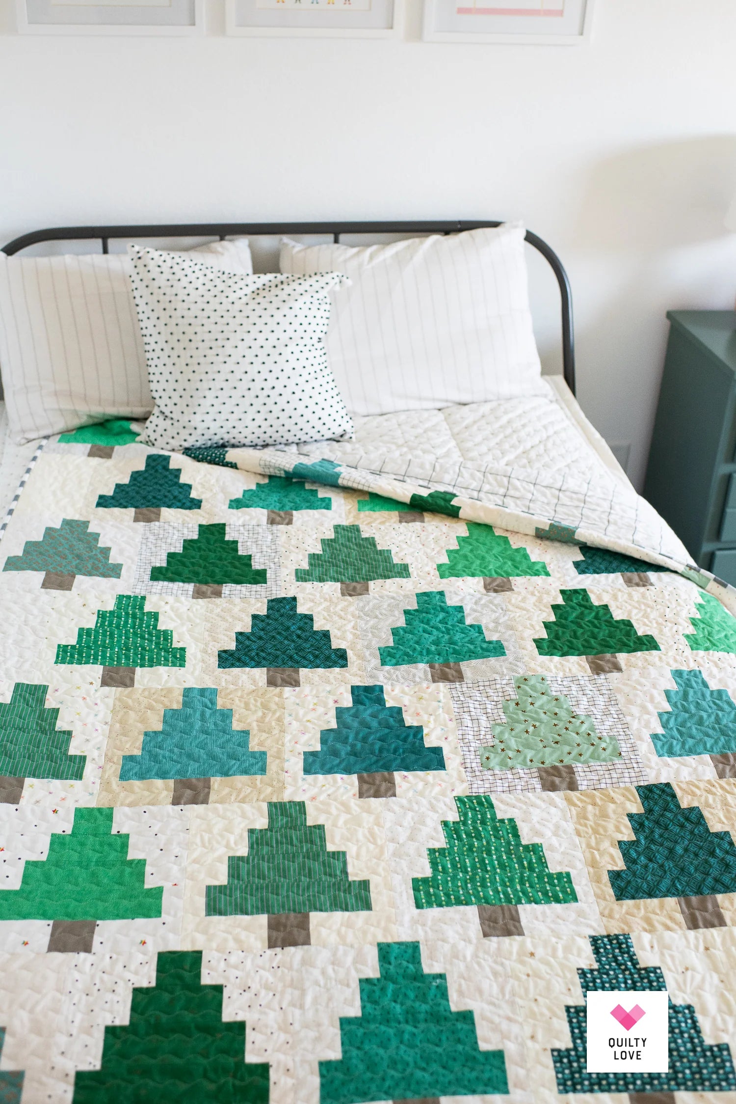 A quilted bedspread featuring a green tree pattern on a cream background, styled on a bed with white pillows in a bright bedroom.
Photo by Quilty Love [additional_image_link]
