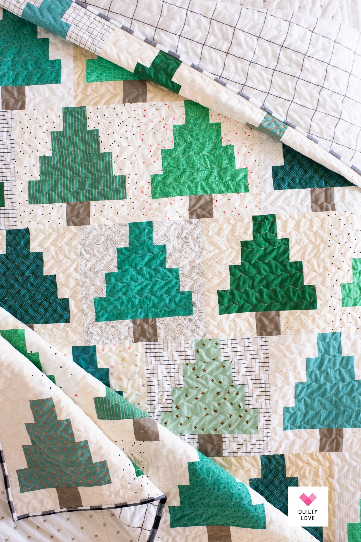 A quilted blanket featuring a pattern of green Christmas trees on a cream background with subtle tiny dots, folded to show the reverse side with a grid pattern.
Photo by Quilty Love [additional_image_link]