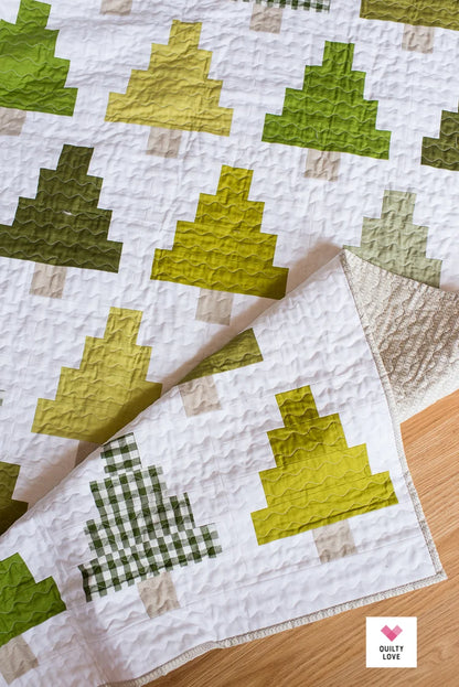 Quilt with green and brown geometric pattern on a wooden surface.
Photo by Quilty Love [additional_image_link]