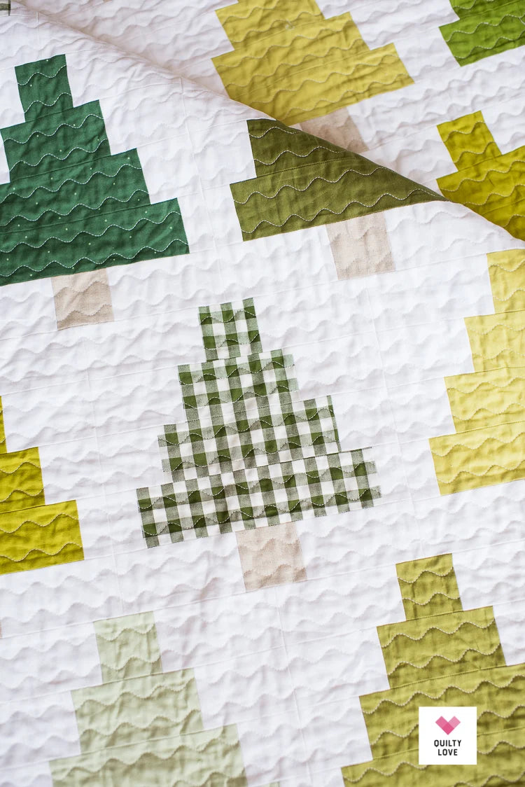 A close-up of a quilted textile with a white base and stitched tree motifs in dark green, olive green, pale yellow, and light beige. A small 'Quilty Love' logo appears in the bottom-right corner.
Photo by Quilty Love [additional_image_link]