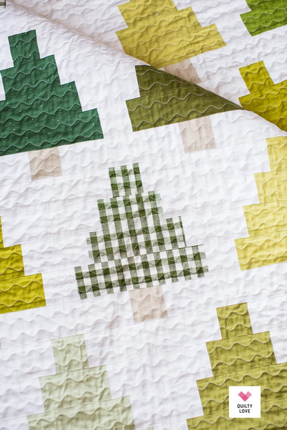 A close-up of a quilted textile with a white base and stitched tree motifs in dark green, olive green, pale yellow, and light beige. A small 'Quilty Love' logo appears in the bottom-right corner.
Photo by Quilty Love [additional_image_link]