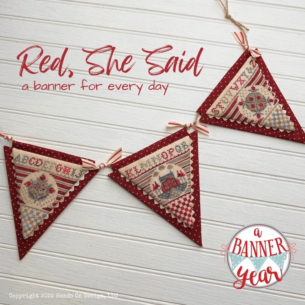 Three red fabric triangular hanging banners with stitched holiday motifs and text, displayed against a white wood plank background. Large red script text reads 'Red, She Said a banner for every day,' and a circular logo in the lower right says 'a BANNER year'.
Photo by Hands on Design [image_link]