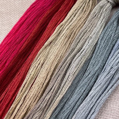 Four skeins of embroidery floss in vertical stripes of bright pink, rust red, warm beige, and dusty blue, laid diagonally on a textured beige fabric background.
Photo by Hands on Design [additional_image_link]