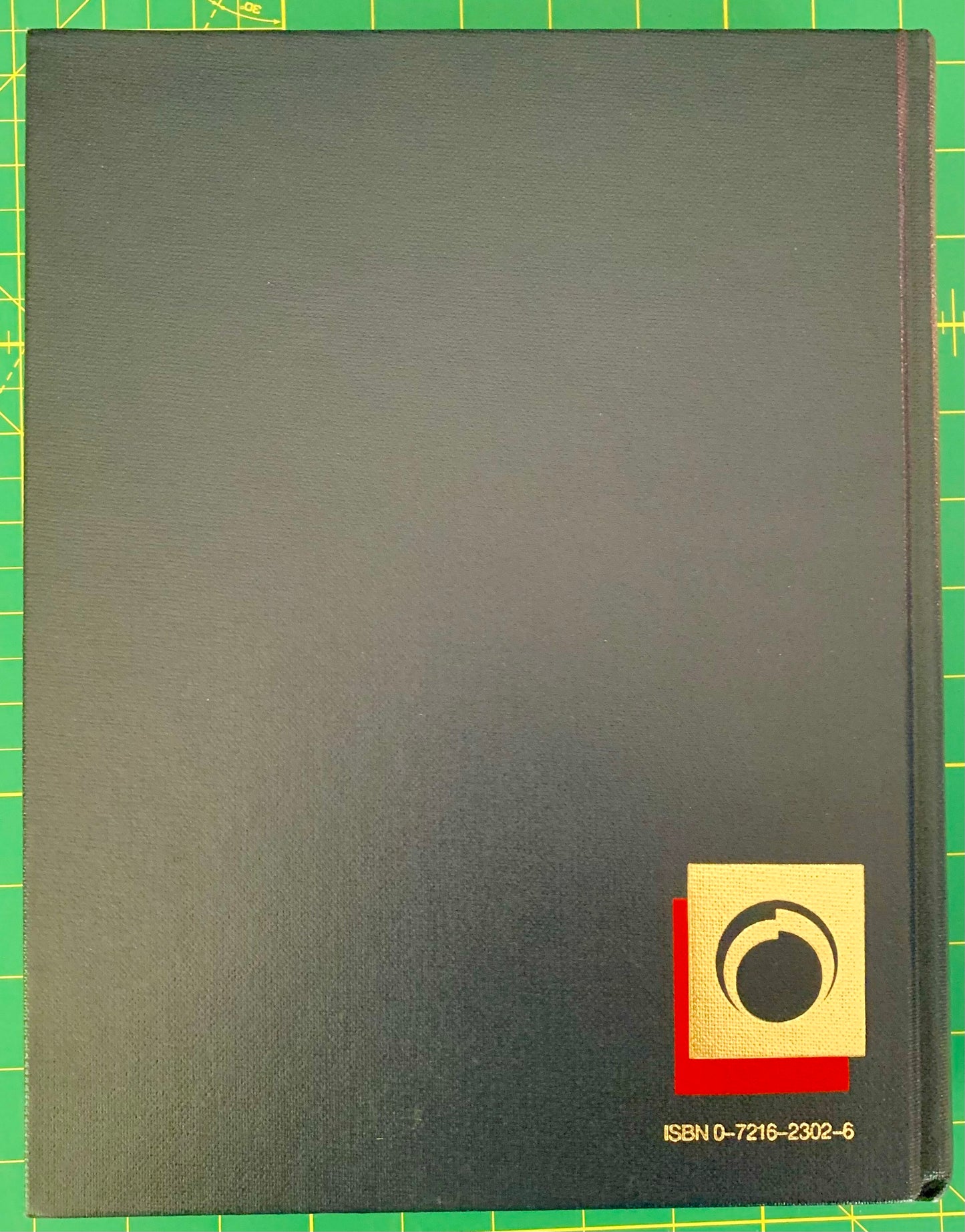 A dark blue hardcover book cover placed on a green cutting mat with yellow grid lines. The cover features a small gold square logo with a black circular motif and red accent, along with the ISBN number 0-7215-2302-6 in the bottom right corner.
[additional_image_link]