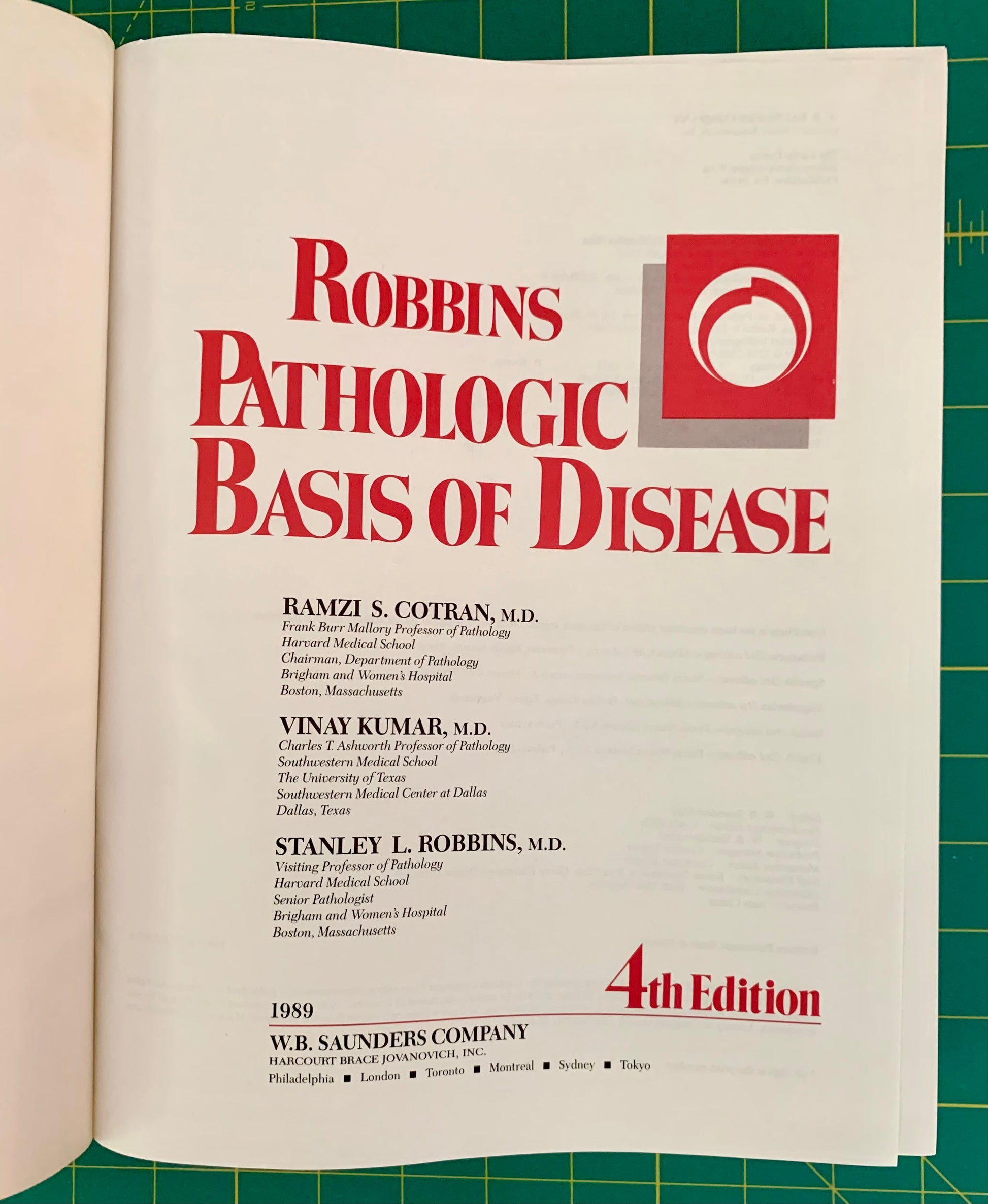 An open book showing the title page of Robbins Pathologic Basis of Disease, 4th Edition, with large red title text on a white page against a green cutting mat background.
[additional_image_link]