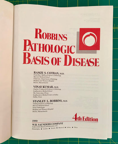 An open book showing the title page of Robbins Pathologic Basis of Disease, 4th Edition, with large red title text on a white page against a green cutting mat background.
[additional_image_link]