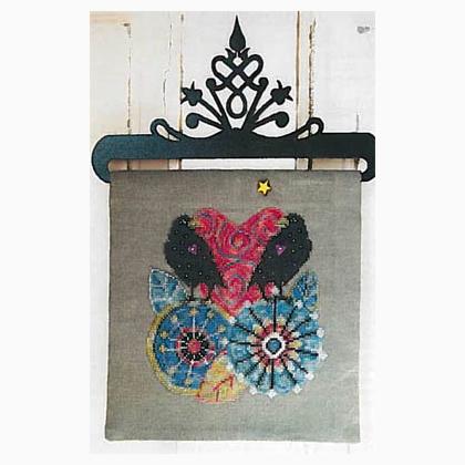 A decorative textile wall hanging or tapestry with a gray fabric panel featuring a colorful embroidered or beaded butterfly design, suspended from a black metal hanger against a white wood plank background.
Photo by SamSarah Studio Designs [additional_image_link]