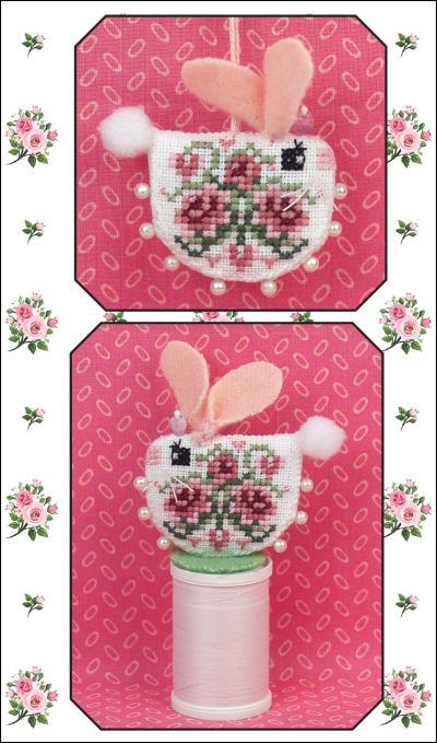 A cross stitch embroidery pattern of a bunny with pink ears and a fluffy tail, adorned with roses and hearts in shades of pink, on a pink background. The pattern includes a color cover and graph for stitching.
Photo by JustNan.com [image_link]