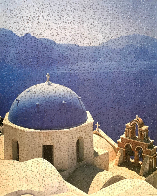 A jigsaw puzzle depicting a scene from Santorini, Greece, with a blue dome structure and mountains in the background.
Photo by Karen King [image_link]