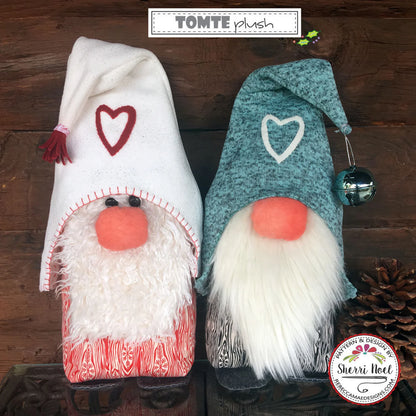 Two plush Christmas gnome decorations displayed side by side on a dark wooden surface. The left gnome wears a white hat with a red heart and a fluffy white beard.
Photo by Sherri Noel [additional_image_link]