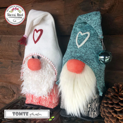 Two handmade fabric gnome ornaments displayed on a dark wooden surface. One gnome has a white hat with a red heart, a red nose, and a white faux-fur beard.
Photo by Sherri Noel [additional_image_link]