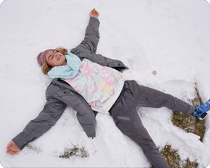 A person lying in the snow making a star angel face, wearing a gray puffer jacket, a pastel tie-dye shirt, a light blue scarf, and a pink knit hat.
Photo by Shannon Fabrics [additional_image_link]