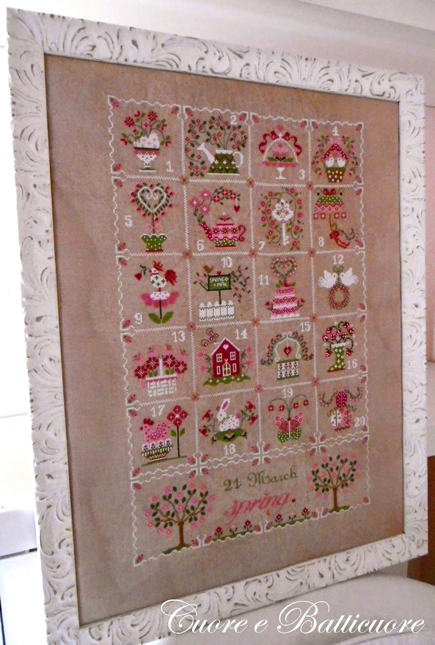 Framed cross-stitched calendar with decorative designs on a beige background.
Photo by CuoreBatticuore.com [additional_image_link]