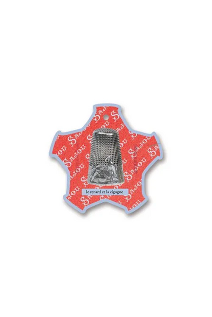 A vintage-style Saint Anthony thread card with a silver-toned metal figure inside a star-shaped glass cover, set against a white fabric background.
Photo by Sajou.fr [additional_image_link]