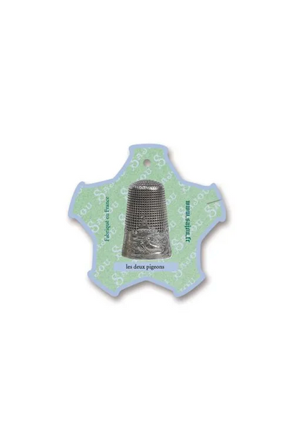 A silver metal thimble displayed on a light green and white decorative thread card, placed on a white background.
Photo by Sajou.fr [additional_image_link]