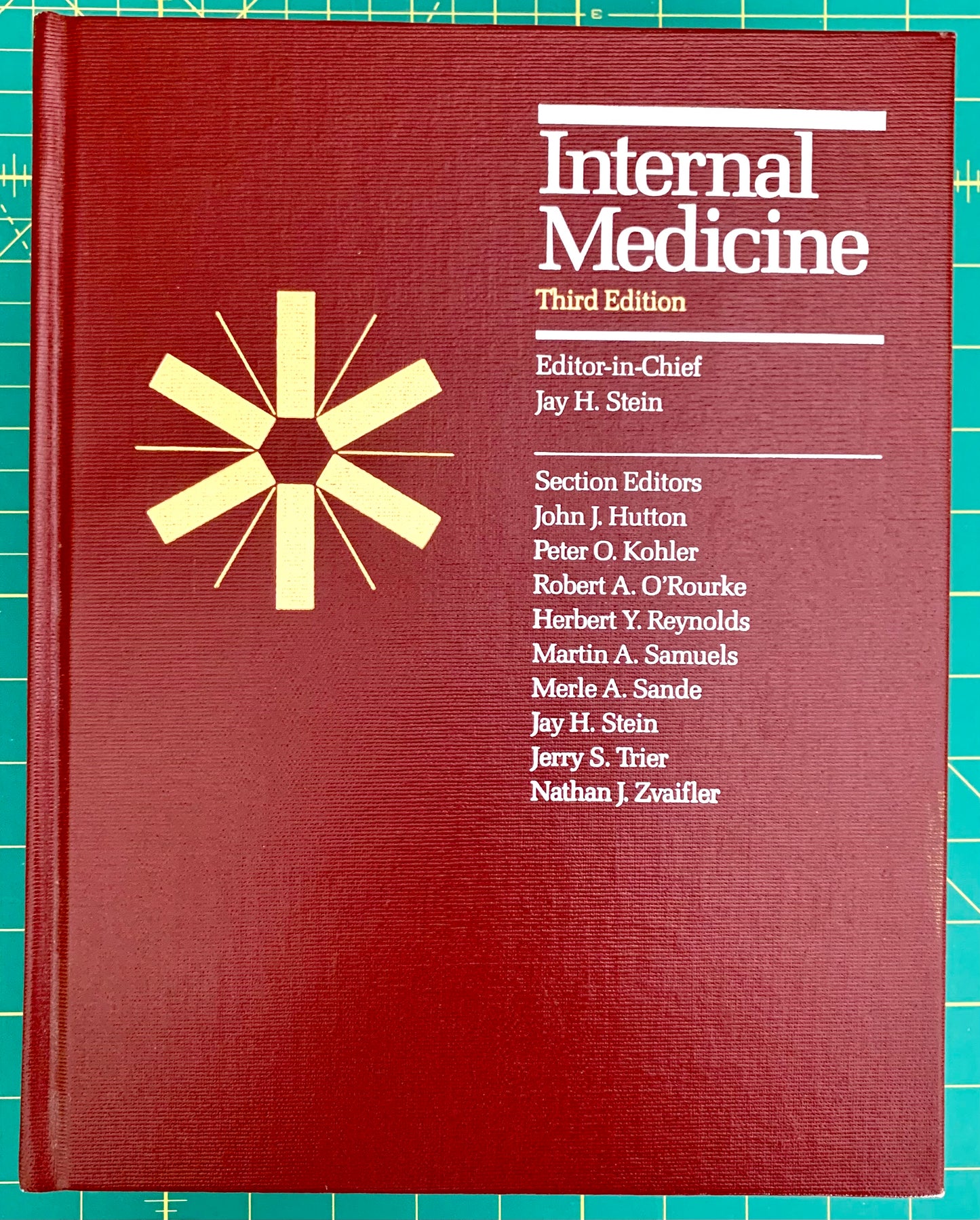 A hardcover book titled 'Internal Medicine Third Edition' with a dark red cover, white text, and a gold starburst emblem, photographed on a green cutting mat background.
[image_link]