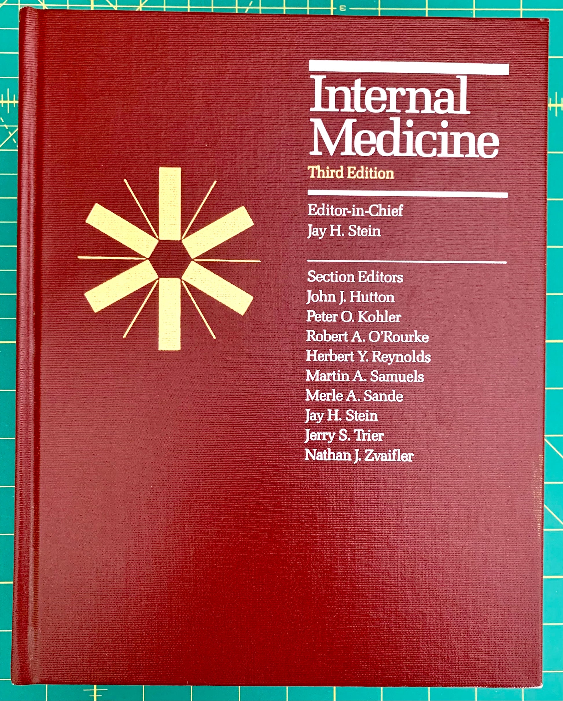 A hardcover book titled 'Internal Medicine Third Edition' with a dark red cover, white text, and a gold starburst emblem, photographed on a green cutting mat background.
[image_link]