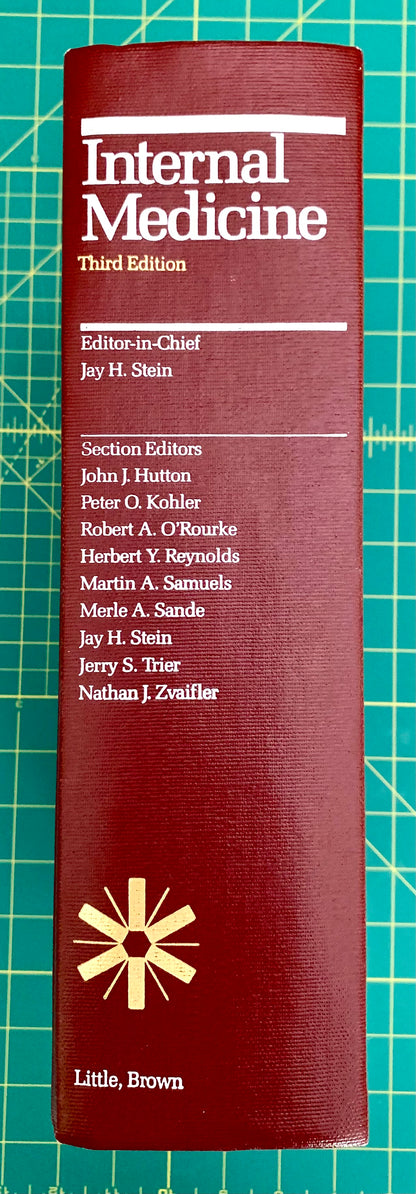 A hardcover book titled 'Internal Medicine, Third Edition' standing upright on a green cutting mat. The cover is dark red/burgundy with white text and a gold starburst logo near the bottom.
[additional_image_link]