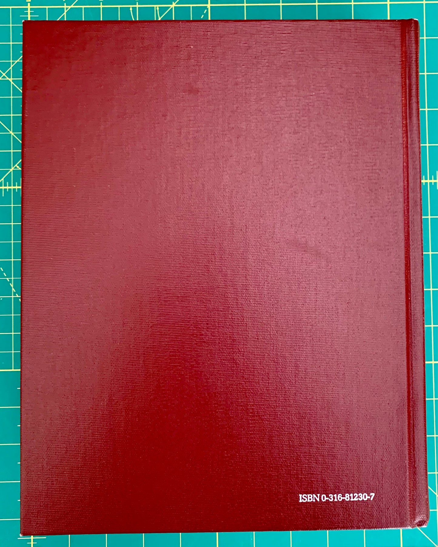 A hardcover book with a textured dark red cover, placed on a green cutting mat with grid lines. The ISBN number 'ISBN 0-315-81230-7' is printed in white at the bottom right corner.
[additional_image_link]