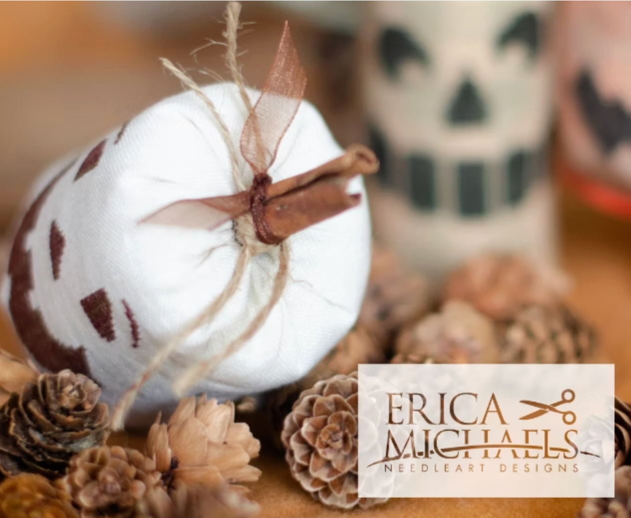 Classic Jack top close up.
A white fabric pumpkin ornament with brown painted spots and a twine stem, styled with pinecones and a cinnamon stick, with a logo overlay for Erica Michaels Needleart Designs.
Photos by Erica Michaels [additional_image_link]