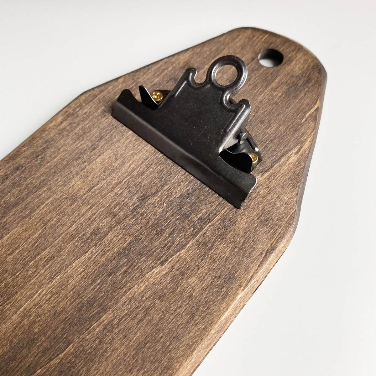 A close-up of a dark brown wooden board with a black metal binder clip attached near the top, set against a plain white background.
Photo by HandsOnDesign.biz [additional_image_link]