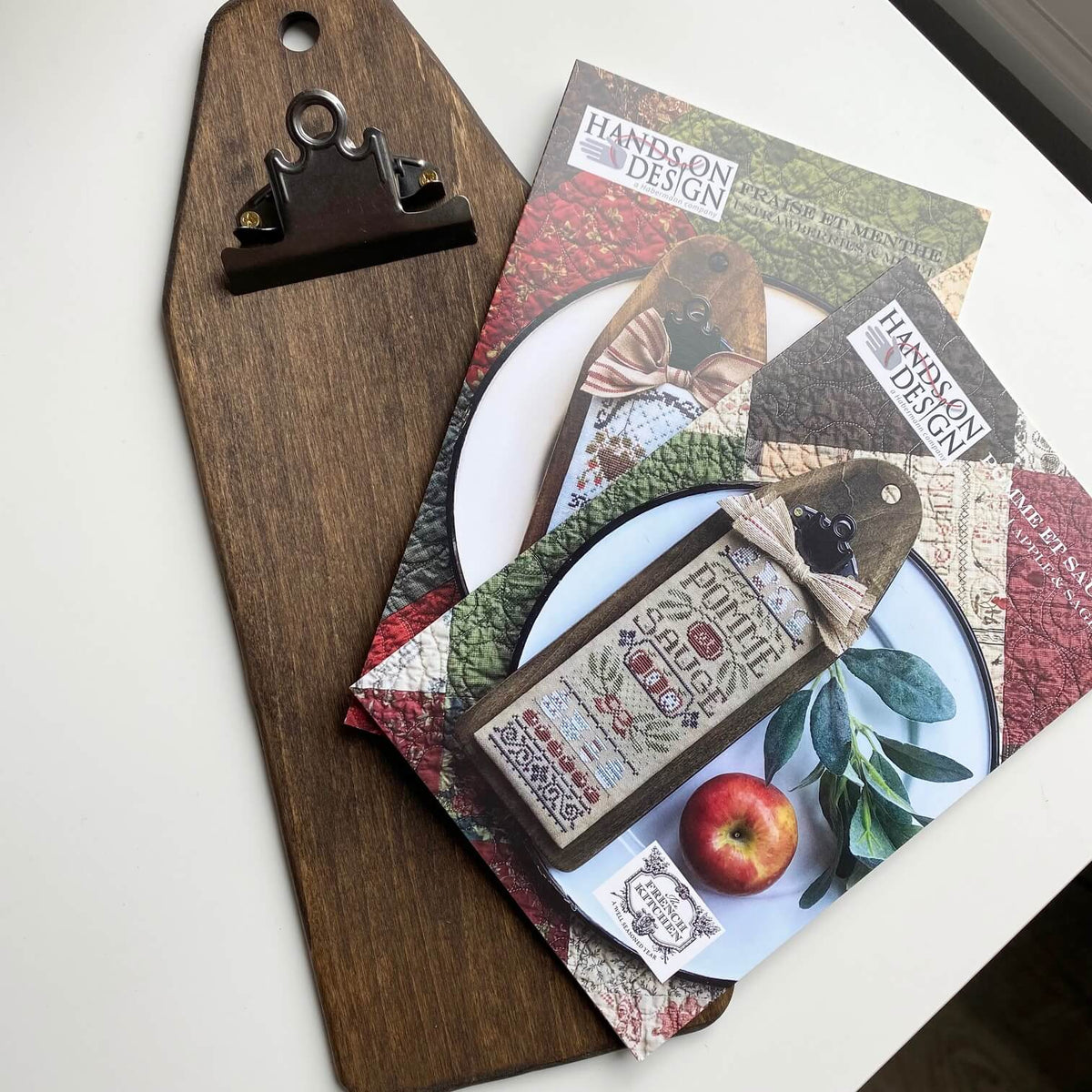 A styled flat-lay of a wooden cutting board with a dark metal clip, featuring printed craft paper sheets and tags with the brand name 'Hands on Design' and rustic autumn-themed illustrations.
Photo by HandsOnDesign.biz [additional_image_link]